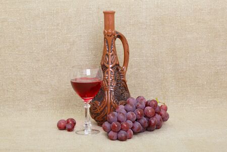 Composition from clay Georgian bottle, a glass and grapes against old canvasの写真素材