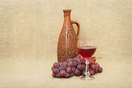 Still-life from a clay bottle, grapes and wine against a canvasの写真素材