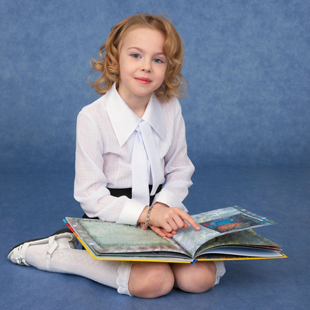 Schoolgirl reading children's book sitting on the floorの写真素材