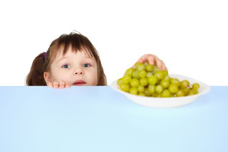 A child reaches for the grapes lying on the tableの写真素材