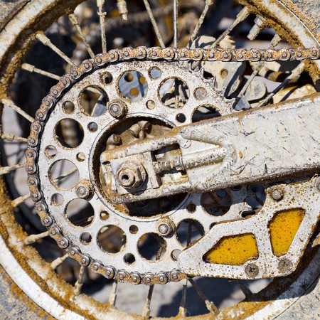 The rear wheel of a motorcycle with a chain, covered with dirtの写真素材