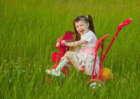 The cheerful little girl goes on a bicycle on a grassの写真素材