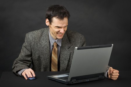 The furious man sits at a table and looks at the laptop screenの写真素材