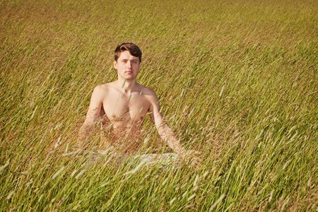 The man sits in a grass in a lotus poseの写真素材