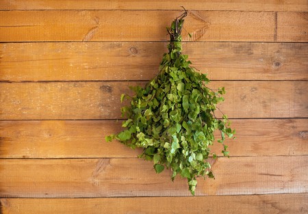The birch broom hangs in a bath on a wooden wallの写真素材