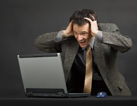 The young man shouts with despair looking at the computer screenの写真素材