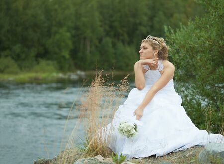 The sad bride sits on river bank and looks afarの写真素材