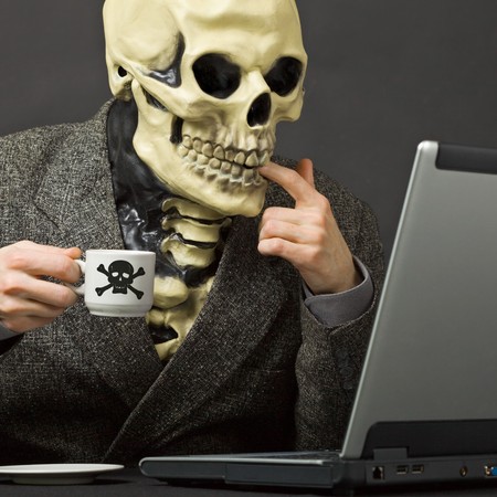 The skeleton drinks poisonous coffee sitting at a table with the laptopの写真素材