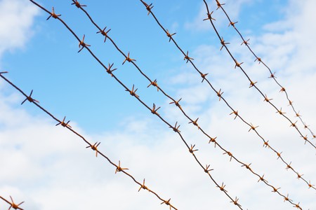 Old rusty barbed wire against the cloudy skyの写真素材