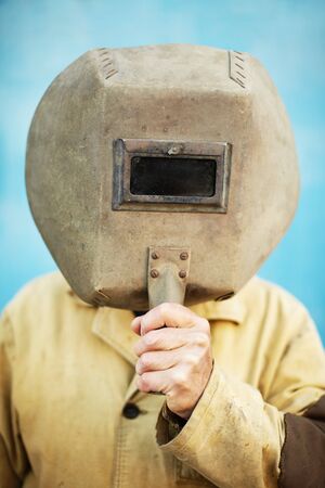 Old welder's helmet in the hands of a welderの写真素材