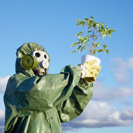 A man in a chemical suit and gas mask with a plant in the handsの写真素材