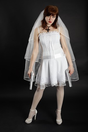 The bride in white dress armed with two pistols on dark backgroundの写真素材