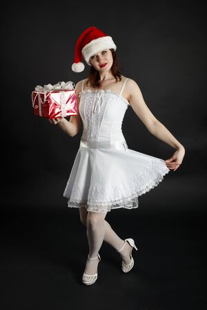 A girl in a red Christmas hat with gifts on dark backgroundの写真素材