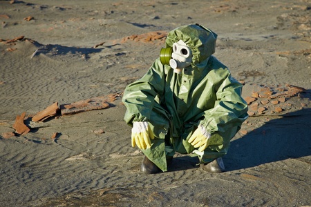 Scientist in a green protective suit and gas mask sitting on the slagの写真素材