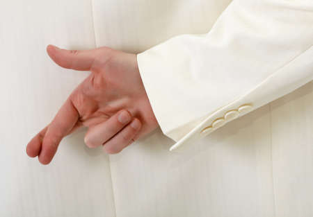 Fingers crossed behind back - man in white suitの写真素材