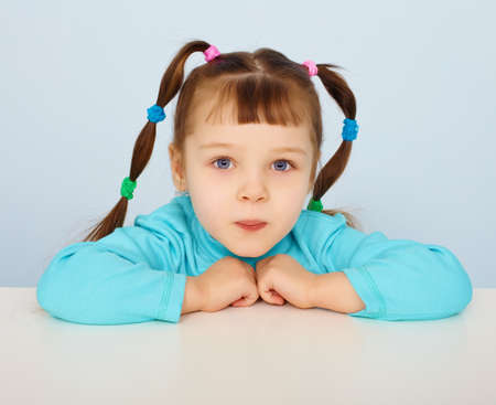 Little girl sitting at a desk on blue backgroundの写真素材