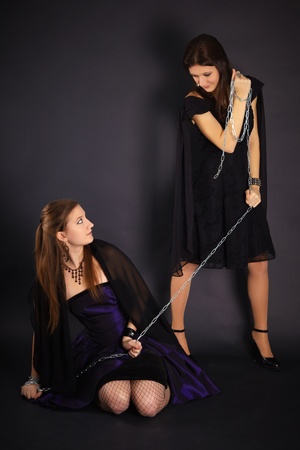 Two young girls playing master and slave on dark backgroundの写真素材