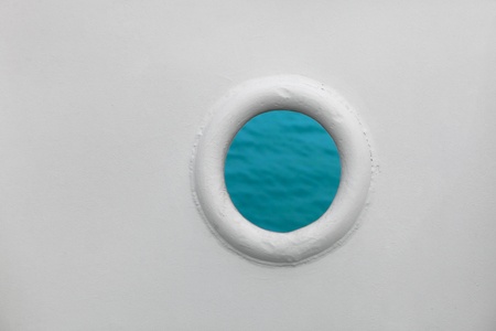 Ship porthole on white wall with blue sea water on backgroundの写真素材