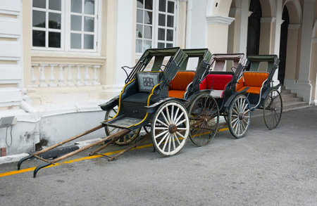 Four classic, old-fashined, manual rickshaws, lined up and waiting for passengers outside a building...