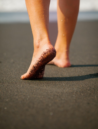 Wet, black sand clings to the bottom of a woman's foot as she strolls along the tropical beach. Bali, Indonesiaの写真素材