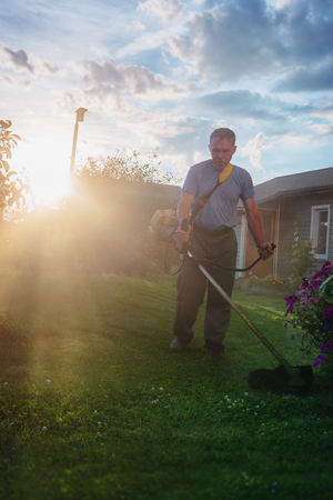 A man mows the grass by trimmer in the gardenの写真素材