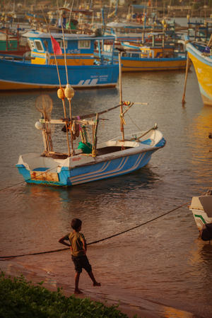 HIKKADUWA, SRI LANKA - CIRCA APR 2013: child near wooden boats in portのeditorial素材