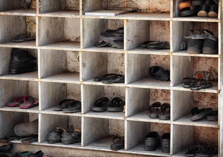 Many pairs of shoes, arranged in old, scuffed and worn cubby holes near the entrance to a Hindu temple in India.の写真素材