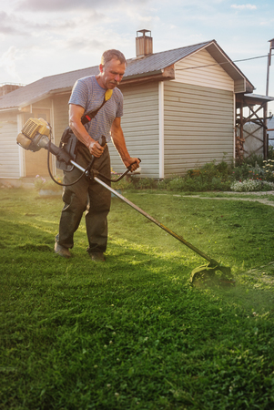 Local homeownter uses a gas powered line trimmer to cut his lawn and edge the sidewalk.のeditorial素材
