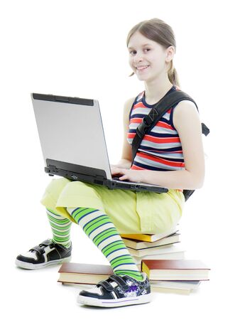 Teen girl smiling in a summer dress with a laptop sitting on the books. White background
の写真素材