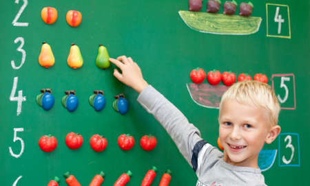 Fresh first year schoolboy student is standing before blackboard during mathematics lesson.の写真素材
