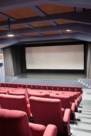Empty cinema auditorium with line of chairs and projection screen. Ready for adding your own picture. Front view.の写真素材