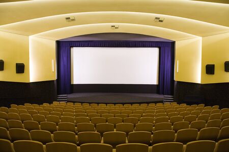 Empty cinema auditorium with line of chairs and projection screen. Ready for adding your own picture. Front view.の写真素材