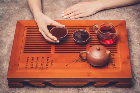 Chinese tea ceremony. The woman holding a cup of tea. Clay teapot with teaware stand on wooden tea table.の写真素材