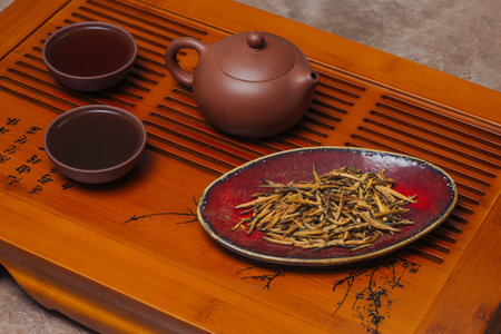Close-up view chinese tea ceremony. Clay teapot, two tea cups and ceramic bowl with red tea stand on wooden tableの写真素材