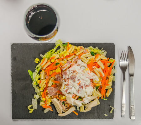 salad with chicken, bacon and pasta sauce logs on a black stone plate with red wine in a glassの写真素材