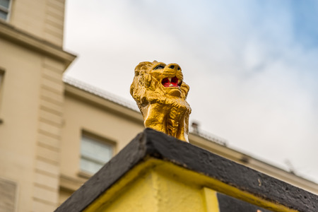 side view on a gold lion on a pedestal in front of the gate to the estate, gold, hand-painted sculpture,  a fantastic decoration in front of the buildingの写真素材