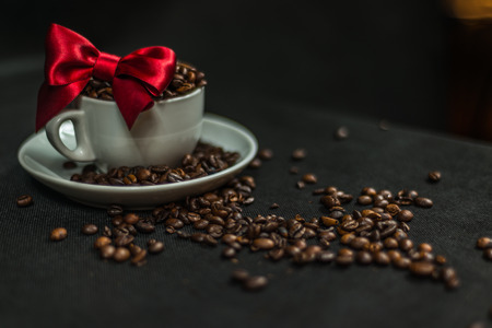 aromatic coffee beans in white cup with decoration of a red bow, spilled coffee beans, artistic decorationの写真素材