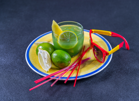 colored drink, a combination of blue and green, decorated with lemon and melon, a glass, a piece of lemon and two limes, yellow and red sunglasses, yellow plateの写真素材