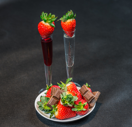 Liqueur and vodka in glasses with strawberries, strawberries with pieces of chocolate on a white saucer, tasty setの写真素材
