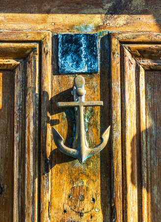 Old wooden door to house with brass knocker shaped like an anchor, sea element, vintage decorの写真素材