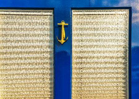 Old wooden door to house with brass knocker shaped like an anchor, sea element, vintage decor