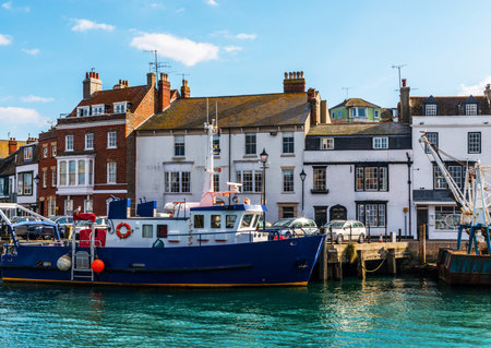 Boats anchored in a small harbor, in the background stone buildings and promenade, seaside