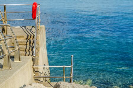 Beautiful blue ocean, part of the promenade with lifebuoy, sunny day, stone wallの写真素材