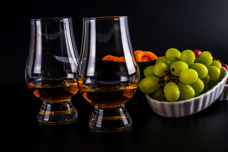 single malt tasting glasses, single malt whisky in a glass, white and red grapes in white bowls, black  backgroundの写真素材
