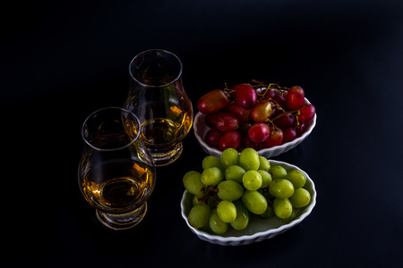 single malt tasting glasses, single malt whisky in a glass, white and red grapes in white bowls, black  backgroundの写真素材