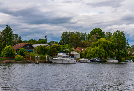 Wide river and houses on the shore, moored boats, green vegetation, a place of relaxation in the city, cloudsの写真素材