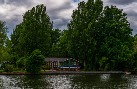 Wide river and houses on the shore, moored boats, green vegetation, a place of relaxation in the city, cloudsの写真素材