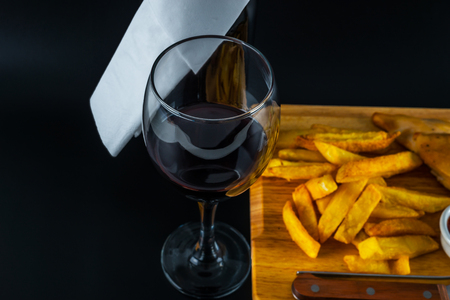 Roast chicken breast with chips, salad with tomatoes and cucumbers, wooden board, knife and fork, black backgroundの写真素材