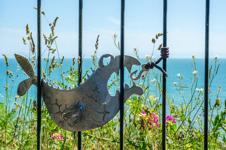 metal ornament on a balustrade in a seaside village, symbolic in the shape of a fish, ocean and...