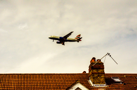 Passenger plane flying over the roofs of residential homes, low airplane flies, red roof tiles, transportationの写真素材